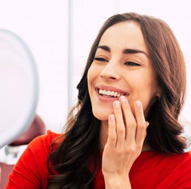 Woman in the dental chair looking in a mirror at her new smile with dental implants in North Attleboro