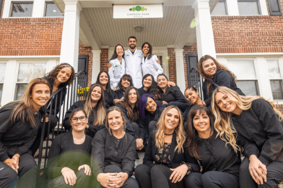Smiling North Attleboro dental team members sitting on the front steps to Capron Park Dental