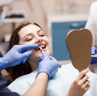 Dentist holding sample veneer to woman’s teeth