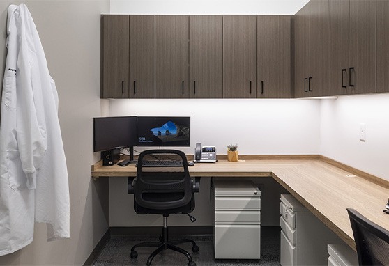 Desk with a computer with a white lab coat hanging on a nearby wall hook