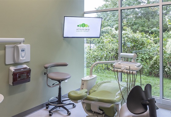 Dental treatment room with a mounted screen on the wall showing the Attleboro Dental Group logo