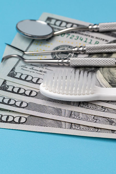 Dental tools and money symbolizing the cost of veneers in North Attleboro